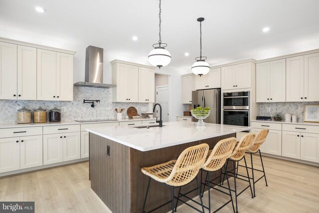 kitchen with a kitchen island with sink, wall chimney range hood, a kitchen bar, and appliances with stainless steel finishes