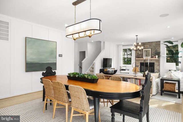 dining area with an inviting chandelier, a stone fireplace, and light hardwood / wood-style floors