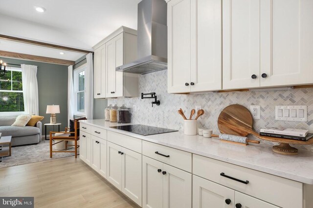 kitchen featuring light hardwood / wood-style flooring, white cabinetry, light stone countertops, black electric cooktop, and wall chimney exhaust hood