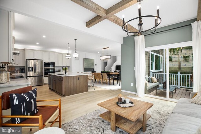 living room featuring beamed ceiling, sink, light hardwood / wood-style floors, and a notable chandelier