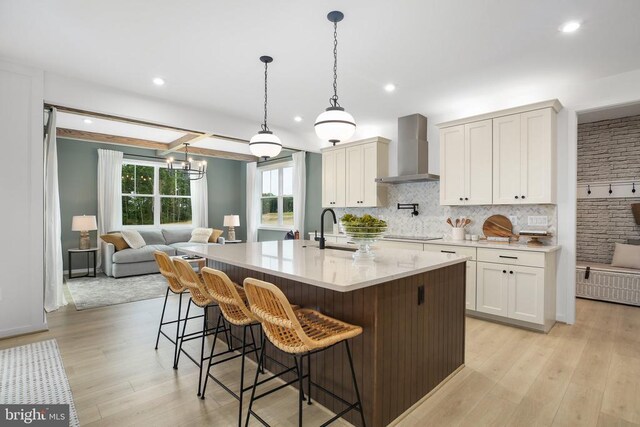 kitchen with wall chimney exhaust hood, a center island with sink, black electric cooktop, pendant lighting, and white cabinets