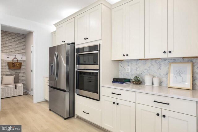 kitchen with tasteful backsplash, white cabinetry, appliances with stainless steel finishes, and light wood-type flooring