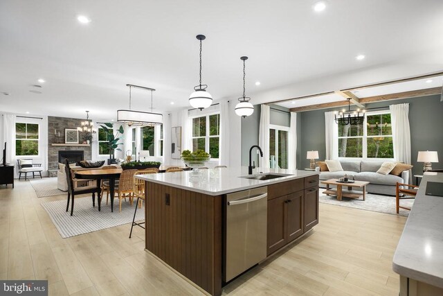 kitchen featuring a stone fireplace, dishwasher, sink, hanging light fixtures, and a center island with sink