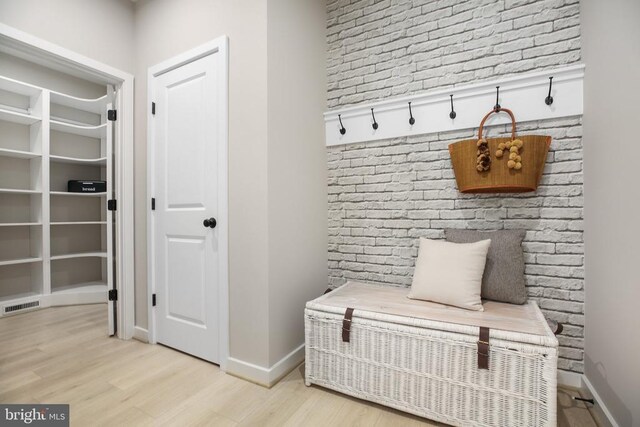 mudroom with brick wall and light hardwood / wood-style flooring