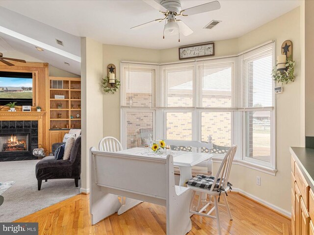 dining space featuring a tiled fireplace, ceiling fan, light hardwood / wood-style flooring, and a healthy amount of sunlight