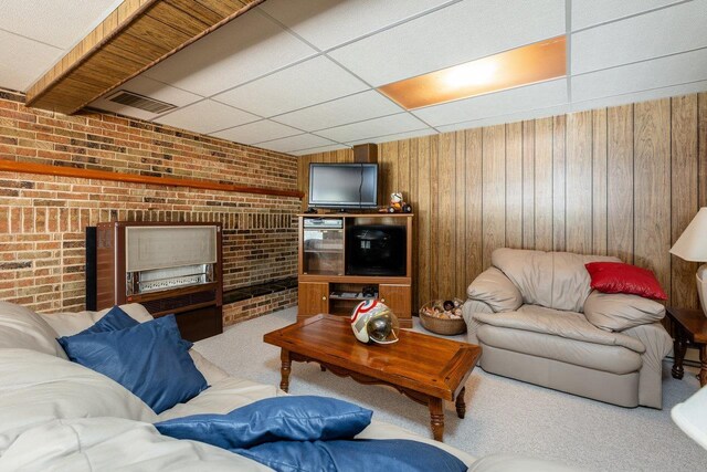 carpeted living room featuring a paneled ceiling, wooden walls, and brick wall