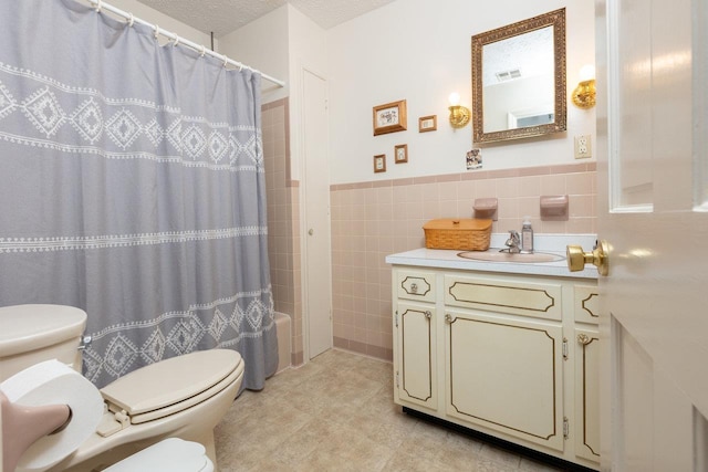 full bathroom with tile walls, vanity, shower / bath combination with curtain, a textured ceiling, and toilet