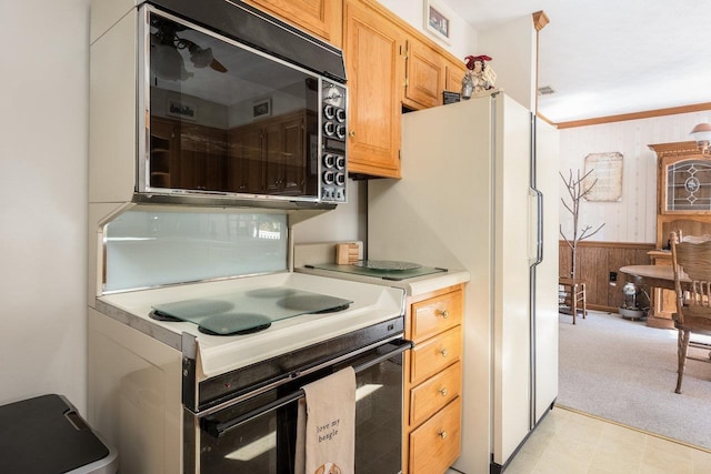 kitchen featuring crown molding, light colored carpet, white appliances, and wood walls