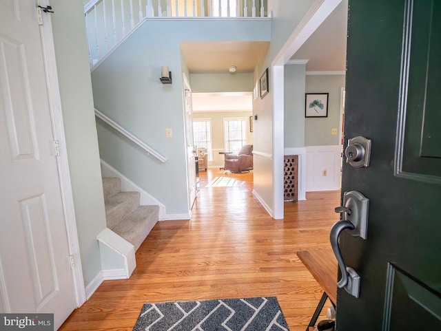 entryway featuring light wood-type flooring, a wainscoted wall, ornamental molding, a decorative wall, and stairs