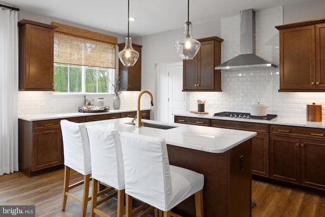 kitchen with sink, a kitchen breakfast bar, stainless steel gas stovetop, a kitchen island with sink, and wall chimney range hood