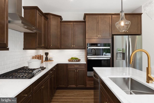 kitchen featuring wall chimney exhaust hood, sink, pendant lighting, stainless steel appliances, and light stone countertops