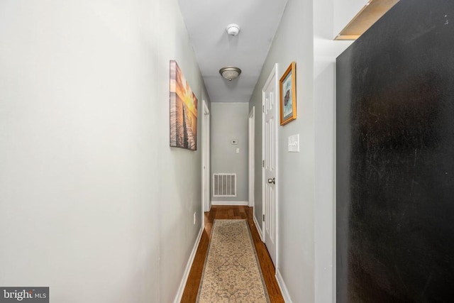 corridor with baseboards, visible vents, and wood finished floors