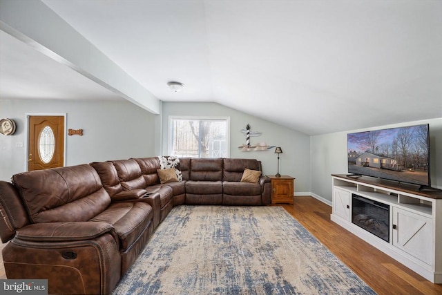 living area with vaulted ceiling, a glass covered fireplace, wood finished floors, and baseboards