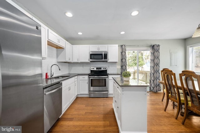 kitchen with stainless steel appliances, white cabinetry, a sink, and wood finished floors