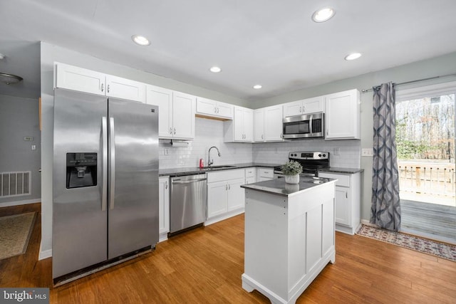 kitchen with wood finished floors, a sink, visible vents, appliances with stainless steel finishes, and dark countertops