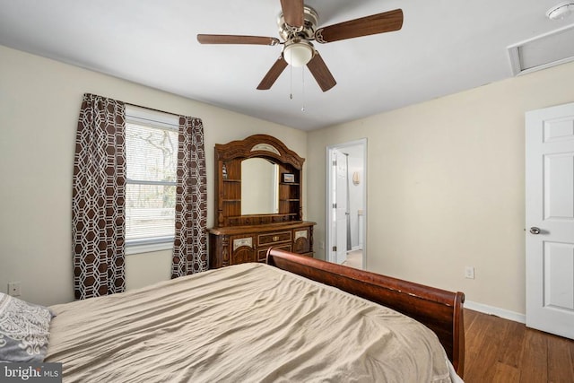 bedroom with ceiling fan, wood finished floors, baseboards, ensuite bath, and attic access