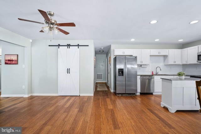 kitchen with a barn door, stainless steel appliances, visible vents, backsplash, and dark wood finished floors