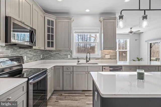 kitchen with decorative light fixtures, sink, backsplash, light hardwood / wood-style floors, and stainless steel appliances