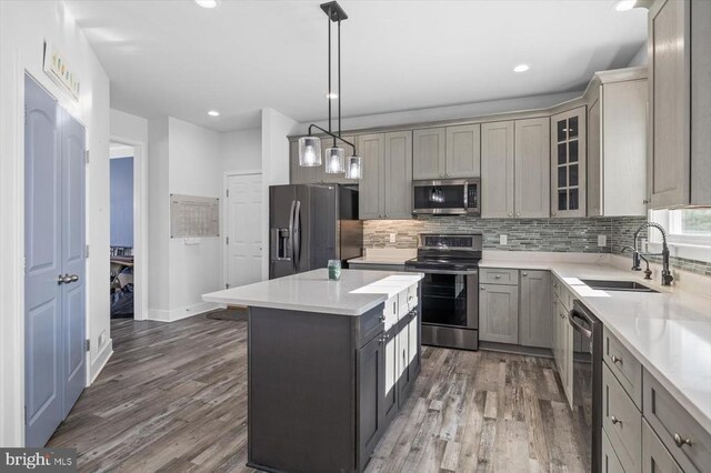 kitchen with dark wood-type flooring, sink, a kitchen island, pendant lighting, and stainless steel appliances