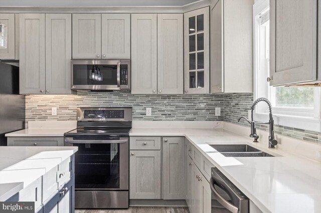 kitchen with appliances with stainless steel finishes, sink, gray cabinetry, decorative backsplash, and light stone countertops