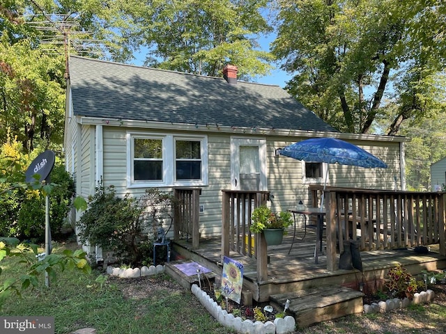 back of property with a shingled roof, a chimney, and a deck