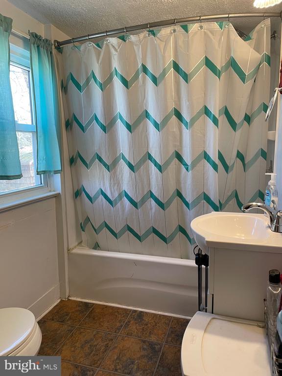 full bath with toilet, vanity, a textured ceiling, and shower / tub combo with curtain