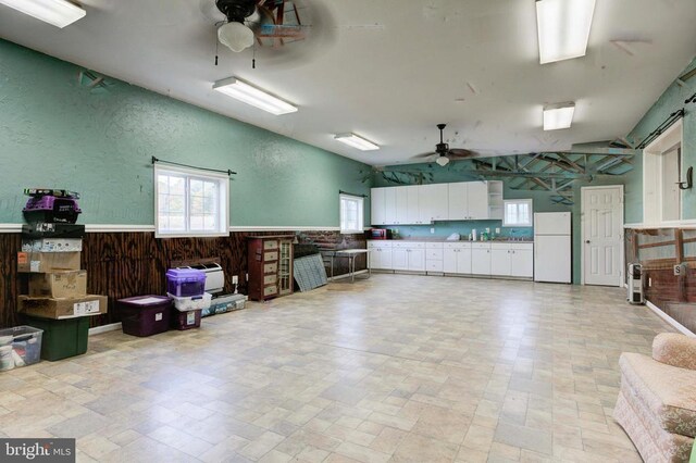 garage with white fridge, wooden walls, and ceiling fan