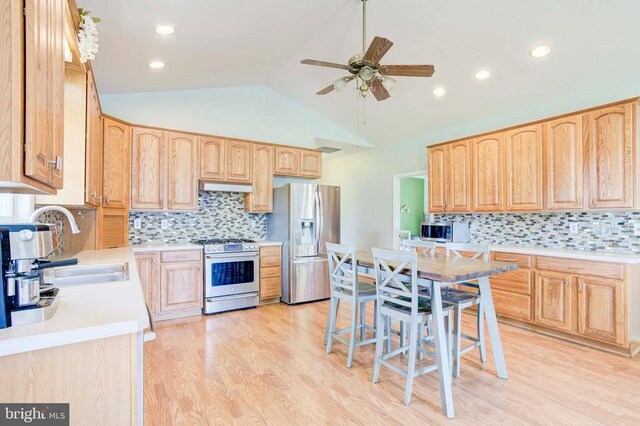 kitchen with vaulted ceiling, appliances with stainless steel finishes, sink, light brown cabinets, and light wood-type flooring