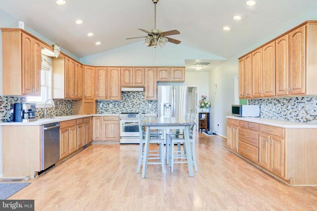 kitchen featuring lofted ceiling, sink, stainless steel appliances, light brown cabinetry, and light wood-type flooring