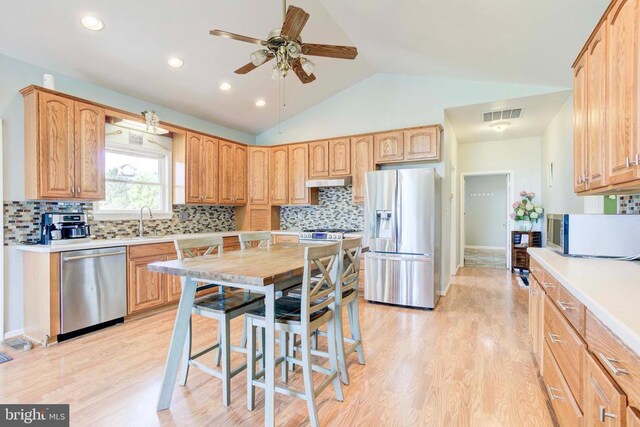 kitchen featuring vaulted ceiling, sink, backsplash, light hardwood / wood-style floors, and stainless steel appliances