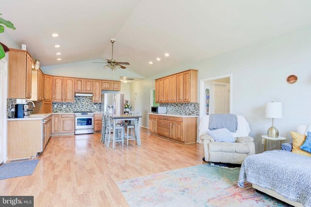 kitchen with vaulted ceiling, stainless steel appliances, a breakfast bar, and light wood-type flooring