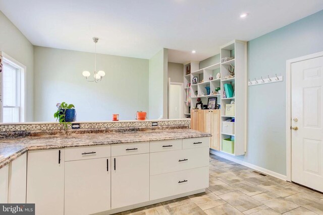 kitchen featuring white cabinetry, light stone counters, pendant lighting, and an inviting chandelier