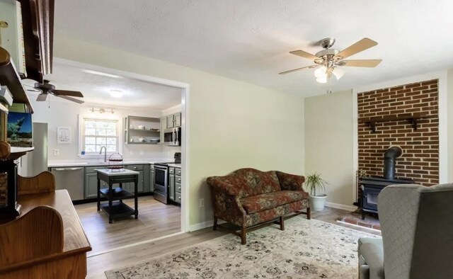 living room featuring sink, a textured ceiling, light wood-type flooring, a wood stove, and ceiling fan