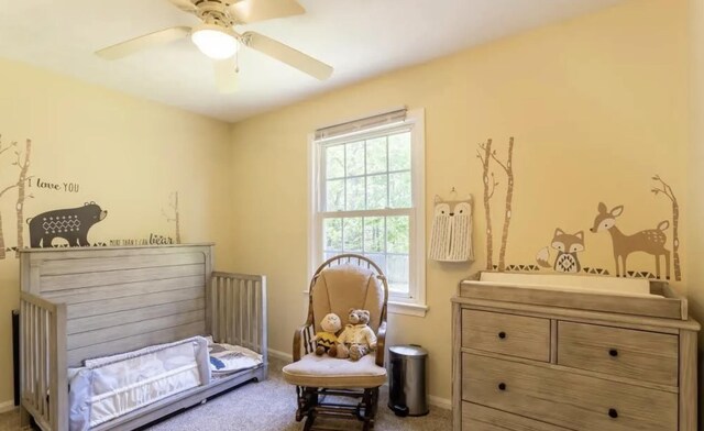 bedroom with a nursery area, carpet, ceiling fan, and baseboards