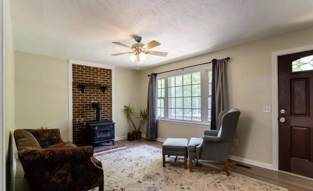 sitting room with hardwood / wood-style flooring, a wood stove, and ceiling fan