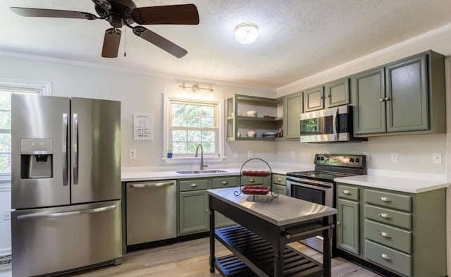 kitchen with sink, green cabinets, stainless steel appliances, ornamental molding, and light hardwood / wood-style floors