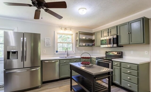 kitchen featuring green cabinetry, appliances with stainless steel finishes, light countertops, crown molding, and a sink