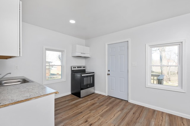 kitchen with stainless steel electric range oven, light wood finished floors, light countertops, white cabinetry, and a sink