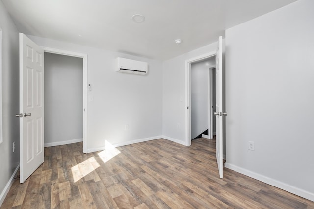 unfurnished bedroom with a wall unit AC, baseboards, and wood finished floors