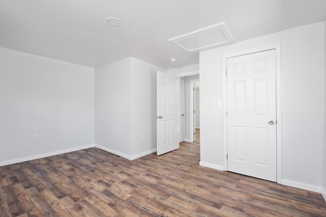 unfurnished room featuring wood finished floors, attic access, and baseboards