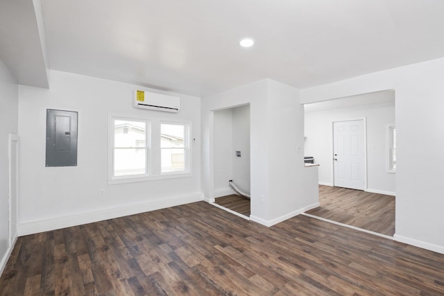 unfurnished room featuring dark wood-style flooring, a wall mounted AC, electric panel, and baseboards