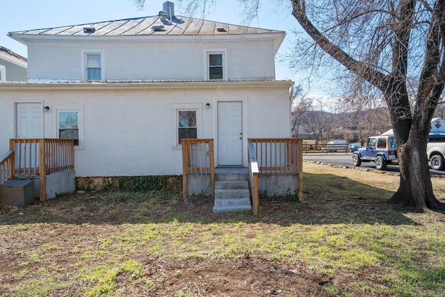 back of house with a standing seam roof, metal roof, a lawn, and stucco siding