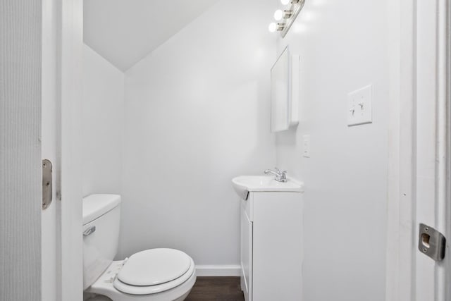 half bathroom featuring baseboards, toilet, wood finished floors, vaulted ceiling, and vanity