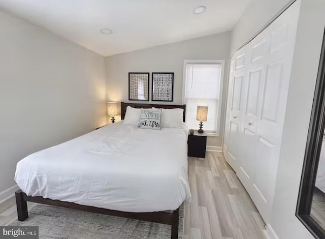 bedroom featuring lofted ceiling, light wood-style floors, baseboards, and a closet