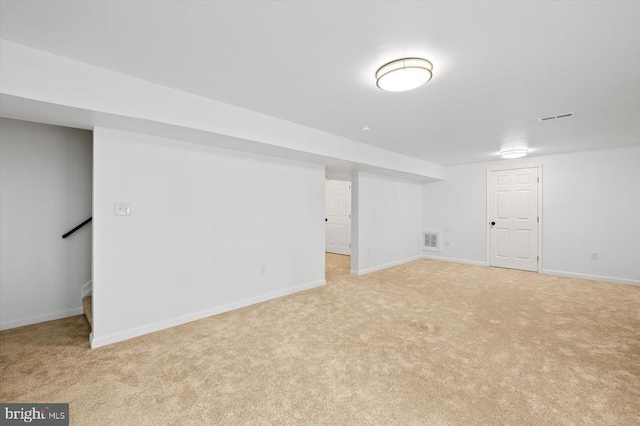 finished basement with stairway, baseboards, visible vents, and light colored carpet