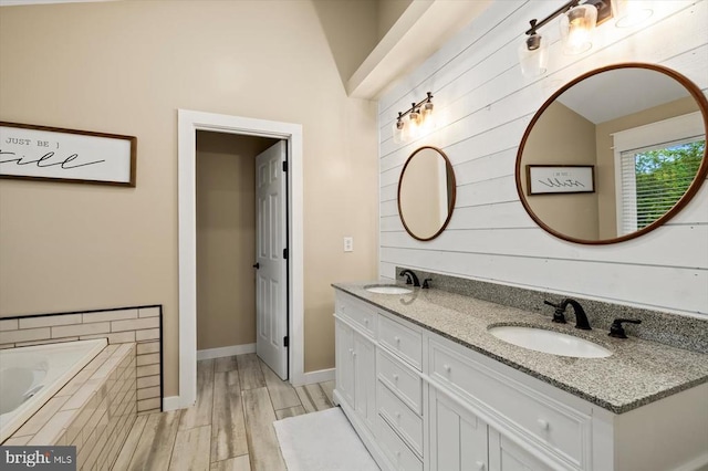 bathroom featuring a sink, tiled tub, double vanity, and wood finished floors