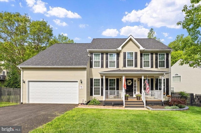 colonial-style house featuring a front lawn, an attached garage, aphalt driveway, fence, and a porch