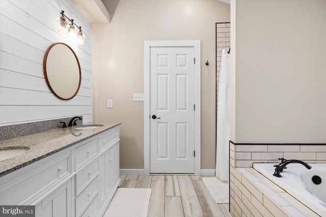full bath with double vanity, baseboards, a relaxing tiled tub, and a sink