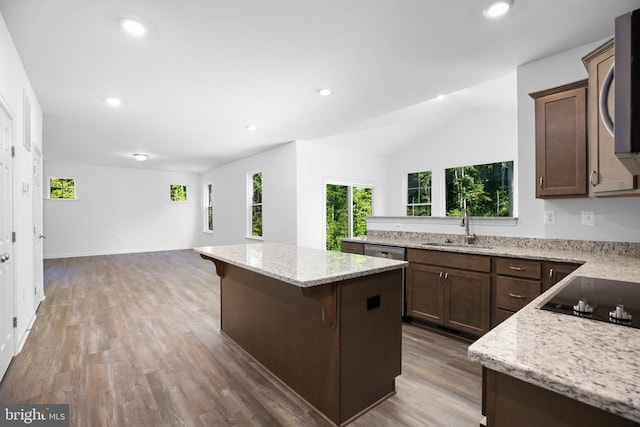 kitchen with sink, stainless steel appliances, a center island, light stone counters, and a kitchen bar