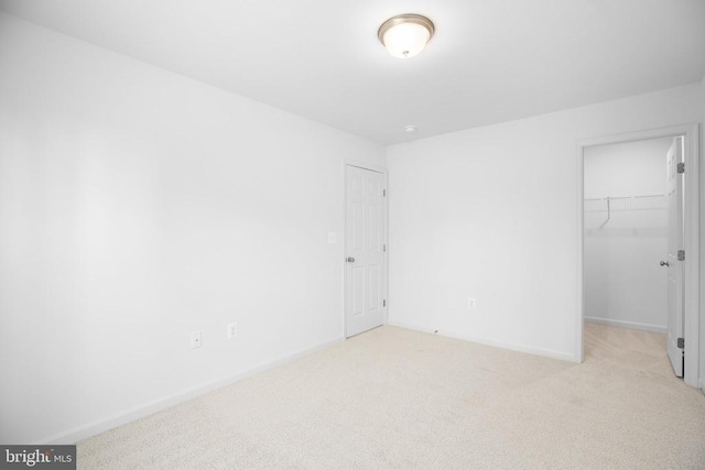 unfurnished bedroom with a spacious closet, light carpet, and a closet